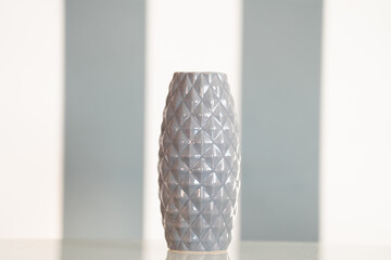 Gray ceramic vase on a white and gray background, placed on a kitchen table as a decorative element