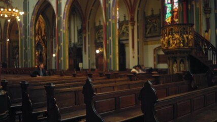 Blurred interior of a catholic church with men sitting on wooden pews, showcasing bokeh effect, stained glass, and ornate decorations creating a serene atmosphere. - Powered by Adobe