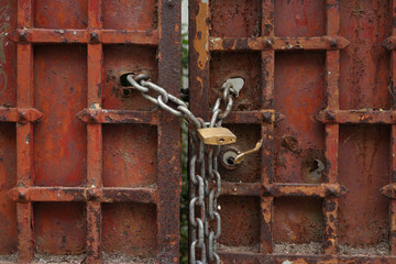 An old padlock with a chain on a rusty entrance gate