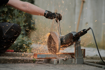 A close-up of a worker using a cut-off saw to cut a metal bar, with bright sparks. A man wearing...