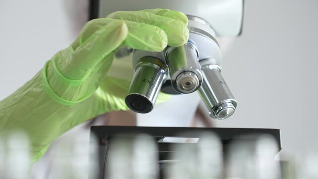 Close up of green gloved hands of a scientist adjusting a microscope in a laboratory, emphasizing the significance of scientific research and analysis. Medicine, healthcare and science concept