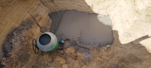 Concrete being poured into a foundation pit with a green cement mixer on a construction site....