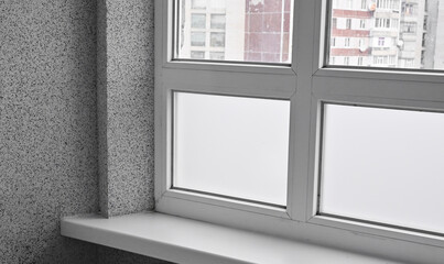Interior shot of double-glazed white window in high-rise building. Urban architecture visible through glass. Window adds brightness and calm atmosphere.