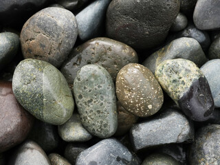 Macro close-up of various smooth wet pebbles in shades of green, brown, black, and grey, highlighting unique patterns and textures.