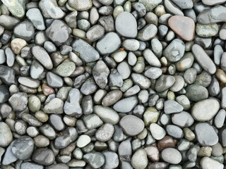 Close-up texture of smooth wet pebbles in various shades of grey, green, and brown, creating a...