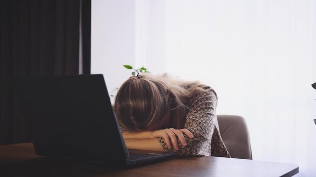 Upset tired woman working on laptop, sitting at table in room, sad girl unemployed freelancer. head sadly falls on hands. depression, bad stress mood fatigue, lack of money. Person looking for job