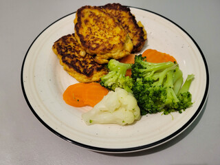 Vegetable fritters are on a plate next to boiled broccoli and carrots.