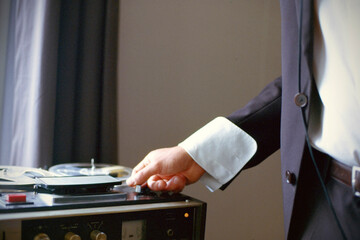 Analog film photograph of person in formal attire operating vintage reel-to-reel tape equipment with atmospheric grain texture