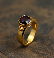 A luxurious gold ring with a stunning ruby red gemstone, set on a dark wood surface. Perfect for a special gift or jewelry collection.
