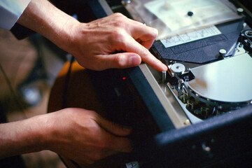 Analog photograph of hands making precise adjustments to vintage audio equipment mechanisms with film grain texture