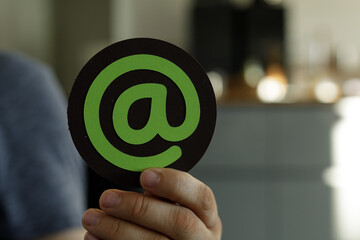 Green at symbol on black circle, held in hand.  Perfect for email, contact, online communication...