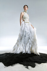 Elegant model in a feathered dress on dark sand.