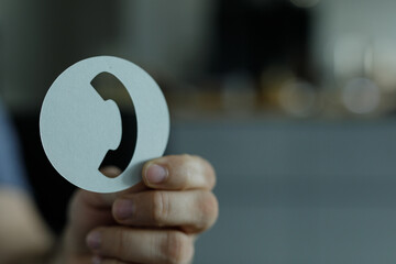 Close-up of a hand holding a circular cutout with a phone symbol.  Perfect for communication,...