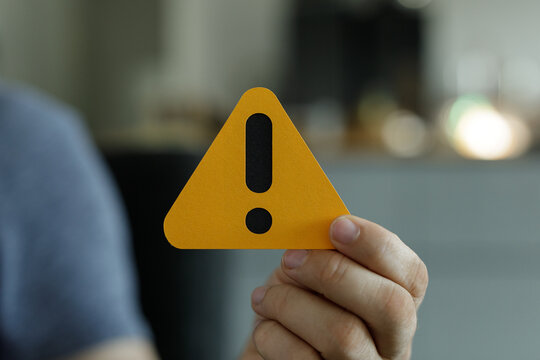 Person holding a yellow triangle warning sign.  Use for caution, alert, or risk concepts.