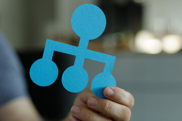 Blue paper cut-out hierarchy chart held in hand.  Illustrates business teamwork, organization, and...