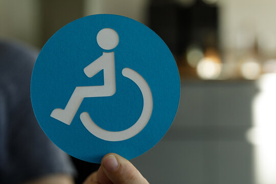 Person holding a blue circle with a white wheelchair accessibility symbol.  Perfect for inclusivity and disability awareness.
