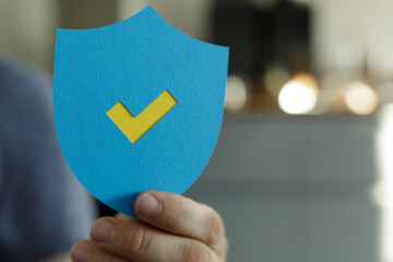 Hand holding blue shield with yellow checkmark.  Security, approval, protection concept.