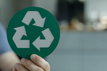 Close-up of a hand holding a circular green sign with a white recycling symbol. Eco-friendly...