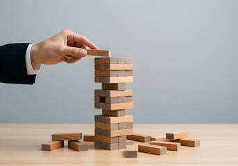 Hand of a businessman building a wooden block tower, a metaphor for business development, managing risk, and strategic planning. Conceptual image about corporate growth, precision, and stability.