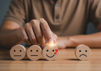 Customer chooses the smiling face with heart eyes icon for a positive review. Concept for excellent customer service satisfaction, feedback survey, and a high-quality rating on wooden blocks.