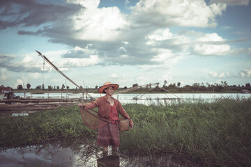 Fisherman Standing in Shallow Water with a Net Surrounded by Lush Greenery and Boat in Background Under a Dramatic Cloudy Sky