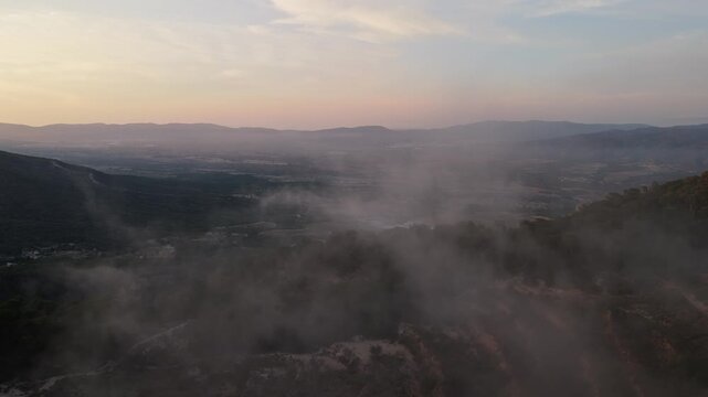 Aerial drone video showing a mist-covered mountain valley in Spain at sunrise, with soft light illuminating the distant hills and open landscape.