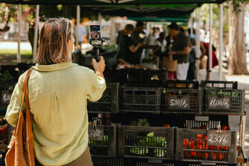 Middle-aged woman blogger filming on the farm market. Mature Female Customer Shopping At Farmers Market Stall. Beautiful woman buying vegetables. Vlogger live streaming. Close up. Part of the series