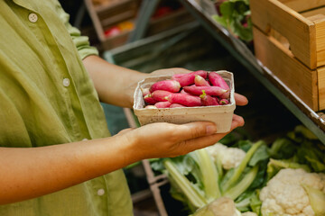 Close up of hand with a radish in shopping basket on the local Farmers market. Mature Female...