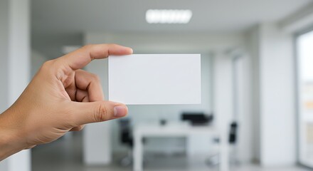 Hand holding a blank white business card mockup against a blurred modern office background.