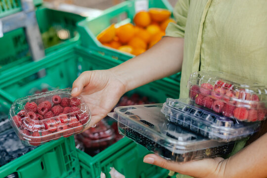 Close-up of hand with fresh berry in plastic packaging at local urban market. Organic produce on sale at outdoor farmer market. Selling fresh crops and veggies harvest. Part of the series