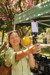 Middle-aged woman blogger filming on the farm market. Mature Female Customer Shopping At Farmers...