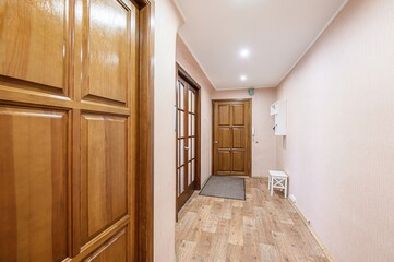 hallway featuring wooden doors, light pink walls, and a wooden-style floor. Overhead lighting illuminates the space