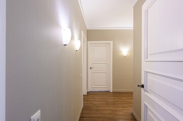 Hallway with white doors, wall lamps, and wooden floors. Neutral color scheme