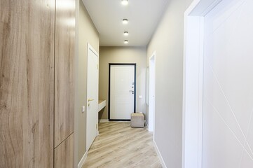 well-lit hallway with wood-look flooring. A large wooden wardrobe is on one side, with white doors and a beige stool visible in the background.  The walls are neutral colored