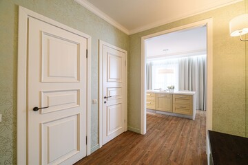 hallway with two white paneled doors and an open doorway leading to a kitchen. Floral wallpaper and wood flooring complete the scene