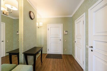 cozy hallway featuring floral wallpaper, wooden floors, and white doors. A dark console table sits against a mirrored wall