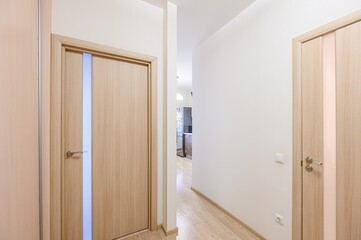 bright hallway view with wooden doors, light walls, and a glimpse of a kitchen in the background