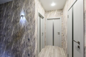 hallway with three light-grey doors, textured wallpaper, light-colored wood flooring, and modern...