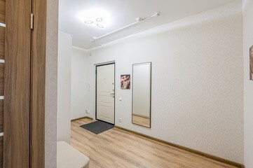 well-lit entryway with a white door, mirror, wood flooring, and patterned wallpaper.  Clean and modern design