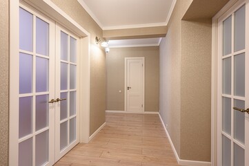 interior shot of a hallway with beige walls, light wood flooring, and white doors, including double...