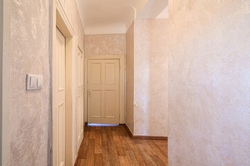 hallway with textured walls and wooden floors. There are two doors on the left side, one slightly...