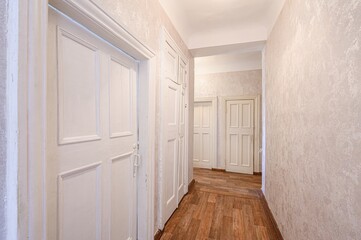 bright hallway with white paneled doors and textured light beige walls. A wood-like floor runs the...