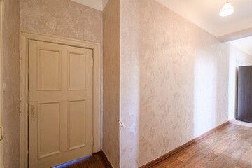 hallway with textured beige walls and wood flooring. A cream-colored door is on the left. A light...