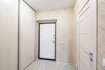 Naklejka premium hallway with a sliding-door wardrobe, a white front door with a black frame, and a light-colored interior door against patterned wallpaper. The floor has gray tiles