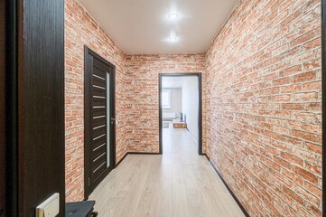 Hallway with brick walls, light wood flooring, and dark wood doors and frames. Open doorway leads to another room