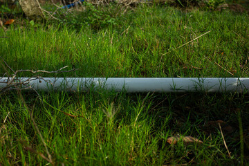 A white PVC water pipe lying on a lush green grass lawn in a garden. Concept of irrigation and water supply systems