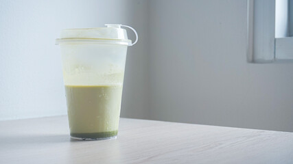 Matcha green tea latte with ice cubes in a transparent plastic cup for takeout isolated on white background. Iced green tea drink