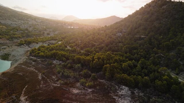 Drone video showing a mountain forest in Spain at sunset, with soft golden light filtering through hills and trees, creating a peaceful and warm atmosphere.