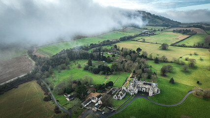 Rolling hills and fields are shrouded by a low-lying cloud formation in a scenic aerial view....