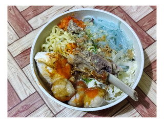 Bakso. A bowl of rib meatballs with yellow noodles, blue vermicelli, shredded cabbage, fried onions and chili sauce on a wooden patterned table. The meatballs look very delicious and delicious.